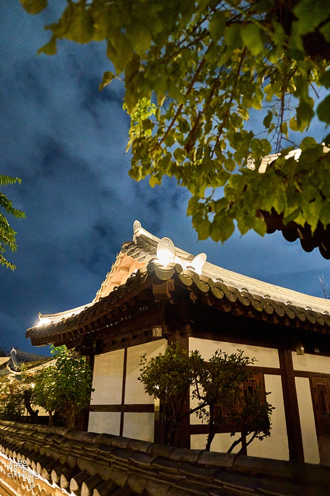 어둠이 내려앉은 푸른 밤하늘 아래 조명을 받아 은은하게 빛나는 한옥의 기와지붕.